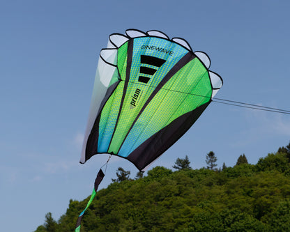 The Aurora Sinewave (blue, yellow and green) in flight with blue sky and trees in the background.